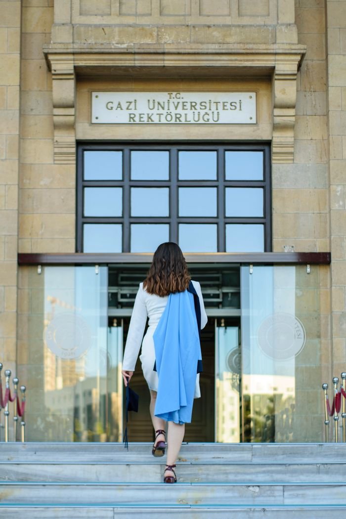 Woman in graduation attire walking into Gazi University entrance, showcasing proud academic achievement.